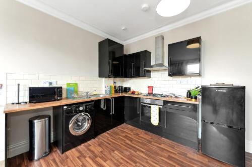a kitchen with black cabinets and a washer and dryer at Derby City Centre, Bright, Spacious, and Airy Apartments - 112 Duffield Road in Derby