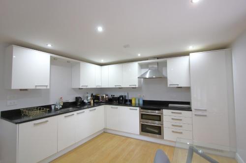 a kitchen with white cabinets and black counter tops at Lovely 2 Bed 2 Bath Flat & Parking by CozyNest in Reading