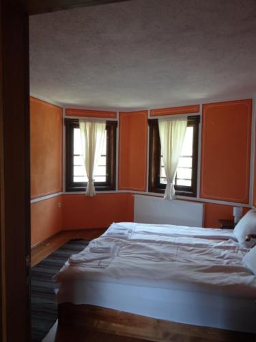 a bedroom with orange walls and a bed with two windows at Недкова къща in Koprivshtitsa