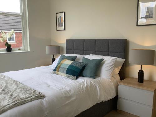 um quarto com uma cama com lençóis brancos e almofadas em Modern 3 bed house in the heart of Morpeth town. em Morpeth
