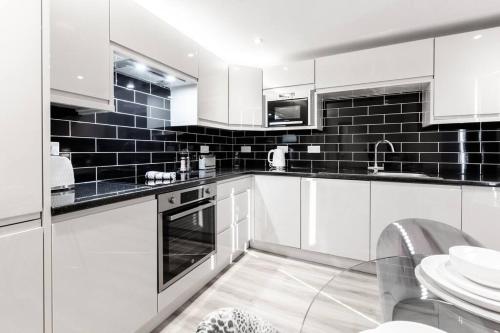 a kitchen with white cabinets and black tiles at Victoria Apt - 2 bedroom Parking Wi-Fi Workers in Hyde