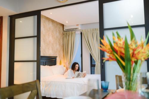 a woman sitting on a bed reading a book at Petronella Suites Apartment @ Jesselton Quay in Kota Kinabalu
