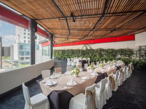 una mesa larga con mesas blancas y sillas en una habitación en The Paragon Hotel Mexico Santa Fe By Accor, en Ciudad de México