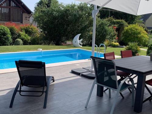a table and chairs with an umbrella next to a pool at Maudon Coeur de Baie in Ponts