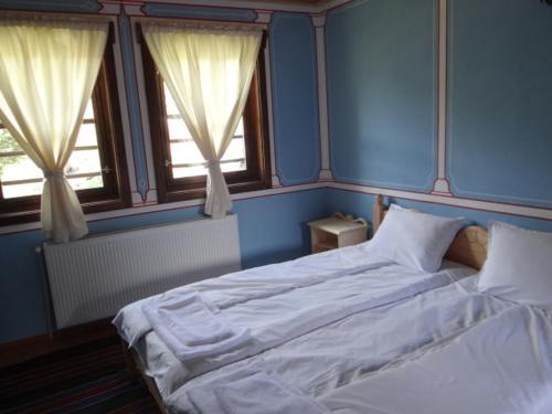 a bedroom with a large bed and two windows at Недкова къща in Koprivshtitsa