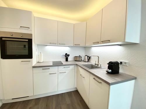 una cocina blanca con armarios blancos y fregadero en Auszeit Apartment STYLE am Uferpark - nur 100 m bis zum Bodensee, direkt am Bodenseeradweg, Sonnenbalkon, schnelles WLAN, kostenloser Tiefgaragenstellplatz, für bis zu 2 Personen, en Friedrichshafen