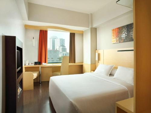 a hotel room with a large bed and a desk at Ibis Jakarta Arcadia in Jakarta