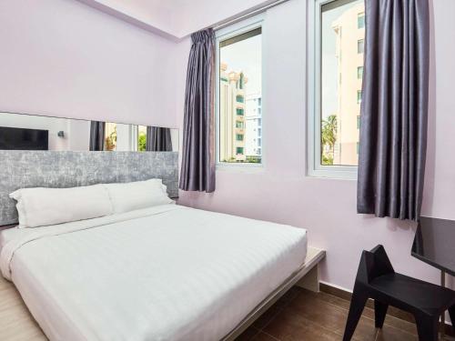 a bedroom with a bed and a desk and windows at ibis budget Singapore Pearl in Singapore