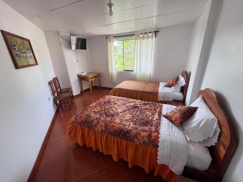 a bedroom with two beds and a table and a window at Hospedaje Familiar Laos in Oxapampa