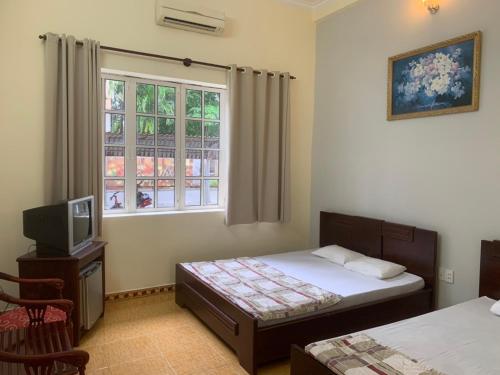 a bedroom with two beds and a tv and a window at Hoang Yen Hotel in Vung Tau