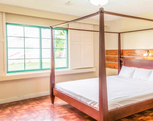 a bedroom with a four poster bed and two windows at Garden Villa Hotel in Tumon