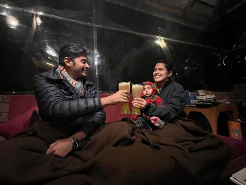 a man and woman holding a glass of beer with a baby at ThePahadians Food & Stay in Jibhi