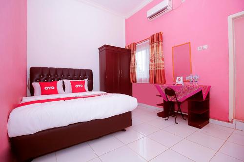 Habitación de color rosa con cama y escritorio de color rosa. en OYO 1847 Jasmine Kost Syariah en Jambi