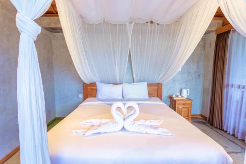 two white wedding towels on a bed with curtains at Kubu D'Carik Villa & Bungalow by ecommerceloka in Munggu