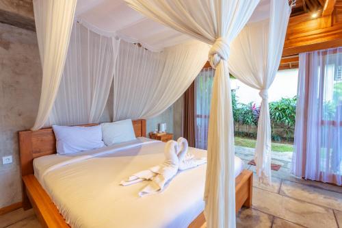 a bedroom with a canopy bed with towels on it at Kubu D'Carik Villa & Bungalow by ecommerceloka in Munggu