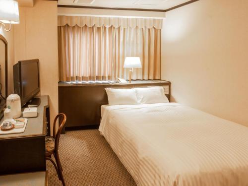 a hotel room with a bed and a desk and a television at Hotel Castle Inn Suzuka in Suzuka