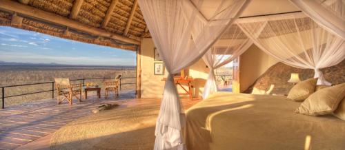 a bedroom with a bed and a balcony with a view at Elewana Elsa's Kopje in Meru