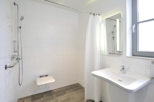 La salle de bains blanche est pourvue d'un lavabo et d'une douche. dans l'établissement ibis De Panne, à La Panne