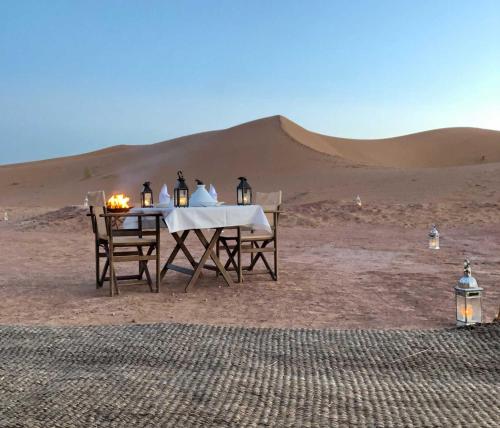 una mesa y sillas en el desierto con una duna de arena en Desert Glamping, en Merzouga