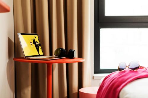 a red table with a laptop on it next to a window at ibis budget Münster City in Münster