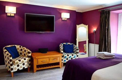 1 dormitorio con paredes de color púrpura, 2 sillas y TV en ALTIDO Charming 3 bed flat in Haymarket, private parking and patio, en Edimburgo