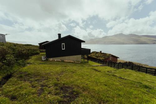 a black house on a hill next to a body of water at Cozy 2-bedroom house with a fantastic view in Leynar
