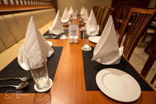 une table en bois avec des assiettes, des verres et des serviettes dans l'établissement BayLeaf Inn, à Port Blair