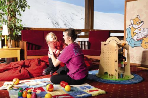 une femme assise sur le sol tenant un bébé dans l'établissement Belambra Clubs Les Menuires - Neige Et Ciel, aux Menuires