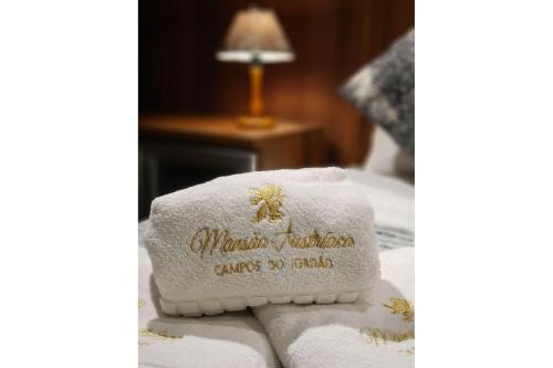 a towel with the name of a hotel on a bed at Mansão Austríaca Guesthouse in Campos do Jordão