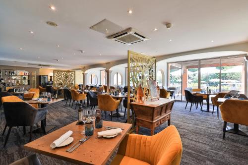 un restaurant avec des tables, des chaises et des fenêtres dans l'établissement Golf Hôtel de Valescure & Spa NUXE, à Saint-Raphaël