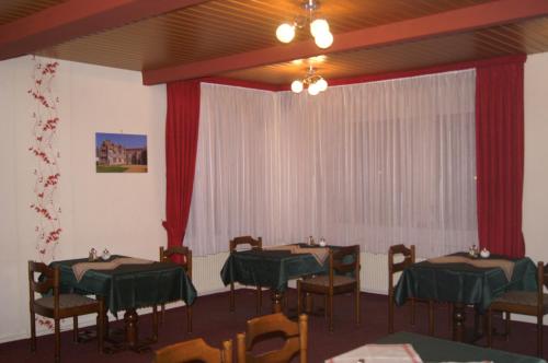 a dining room with two tables and chairs and red curtains at Pension Zur Sonne in Mansfeld