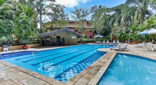 une grande piscine avec chaises et parasols dans l'établissement FLAT AMARILIS RIVIERA DE SÃO LOURENÇO, à Bertioga