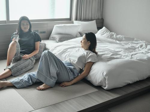 two women sitting on the floor next to a bed at FAV HOTEL HIROSHIMA STADIUM in Hiroshima