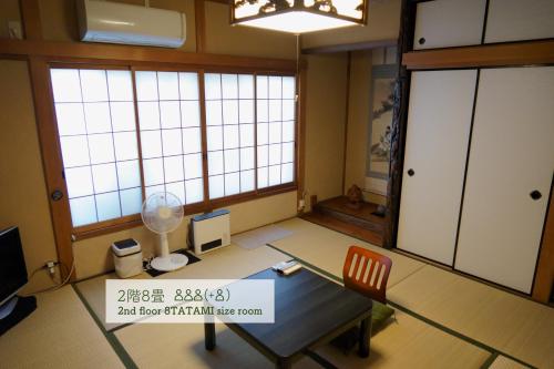 a room with a table and a chair and windows at Guest House Atagoya in Kyoto