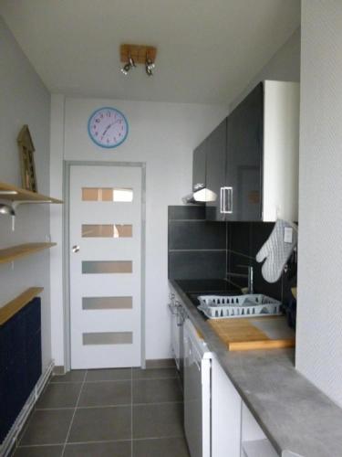 une cuisine avec une horloge sur le mur et une porte dans l'établissement TIANE, à Wimereux