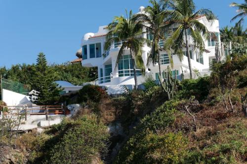 een wit huis op een heuvel met palmbomen bij Hermosa Villa con alberca infinita Playa Zipolite in Puerto Ángel