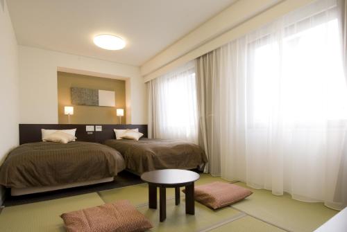 a bedroom with two beds and a table and a window at Dormy Inn Hakata Gion in Fukuoka