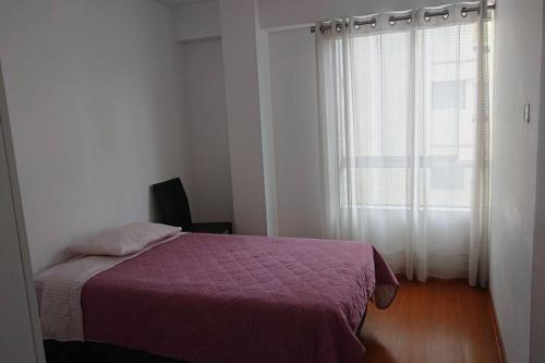 ein Schlafzimmer mit einem Bett mit einer lila Decke und einem Fenster in der Unterkunft Elegante Flat en inmejorable ubicación - San Isidro in Lima