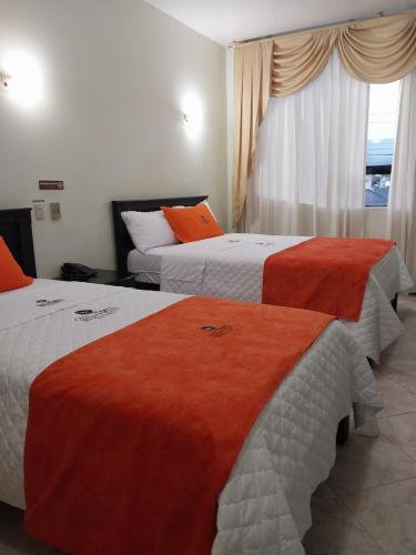 Habitación de hotel con 2 camas con sábanas de color naranja y blanco en Hotel Oro Negro, en Puyo
