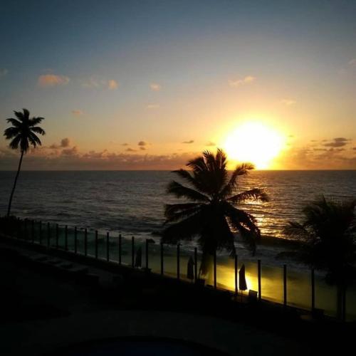 a sunset on the beach with palm trees and the ocean at Flat Tabatinga Nord, vista para o mar in Conde