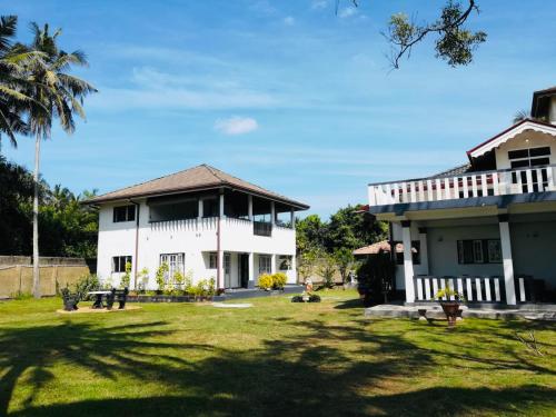 une grande maison blanche avec une cour en herbe dans l'établissement Rosanuka Beach Villa, à Wayikkal