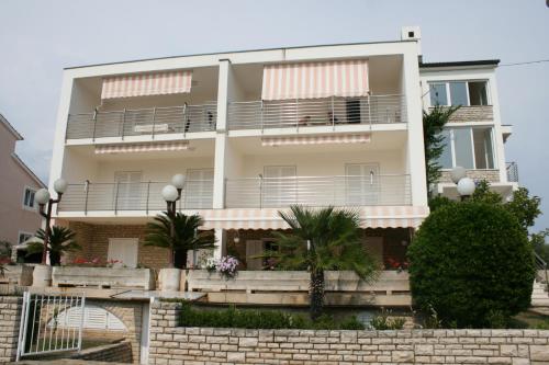 a white building with balconies and palm trees at Apartment Novalja 6398e in Novalja