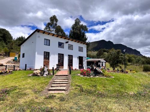 una casa blanca en un campo con montañas en el fondo en Peñavista. en Simijaca