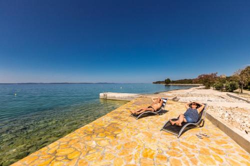 2 personnes assises sur des chaises longues sur la plage dans l'établissement Apartments by the sea Kozino, Zadar - 5755, à Petrčane