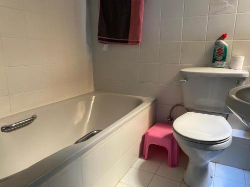 a bathroom with a tub and a toilet with a pink stool at Sea front apartment at Mellieha Bay, Malta! in Mellieħa