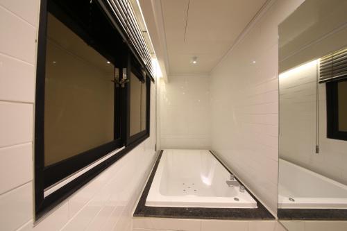 a white bathroom with a tub and a window at Hotel Frenchcode in Busan