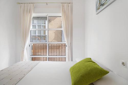 a white bedroom with a green pillow on a bed at Casa Milagros in Sanlúcar de Barrameda