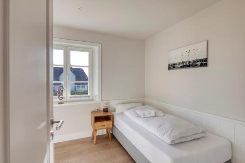 a white bedroom with a bed and a window at Rantum Dorf - Ferienappartments im Reetdachhaus 3 & 4 in Rantum