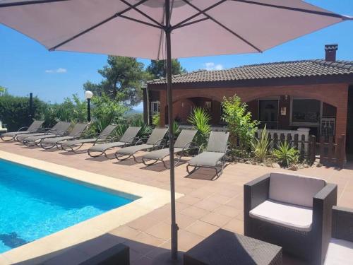 a group of chairs and an umbrella next to a pool at Villa Sitges Soledad 15 minutes drive from Sitges XXL swimming pool 12 p in Olivella