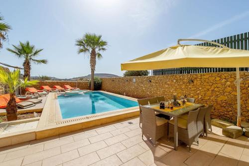 a patio with a table and an umbrella and a pool at Tfiefa Holiday Home in Xagħra